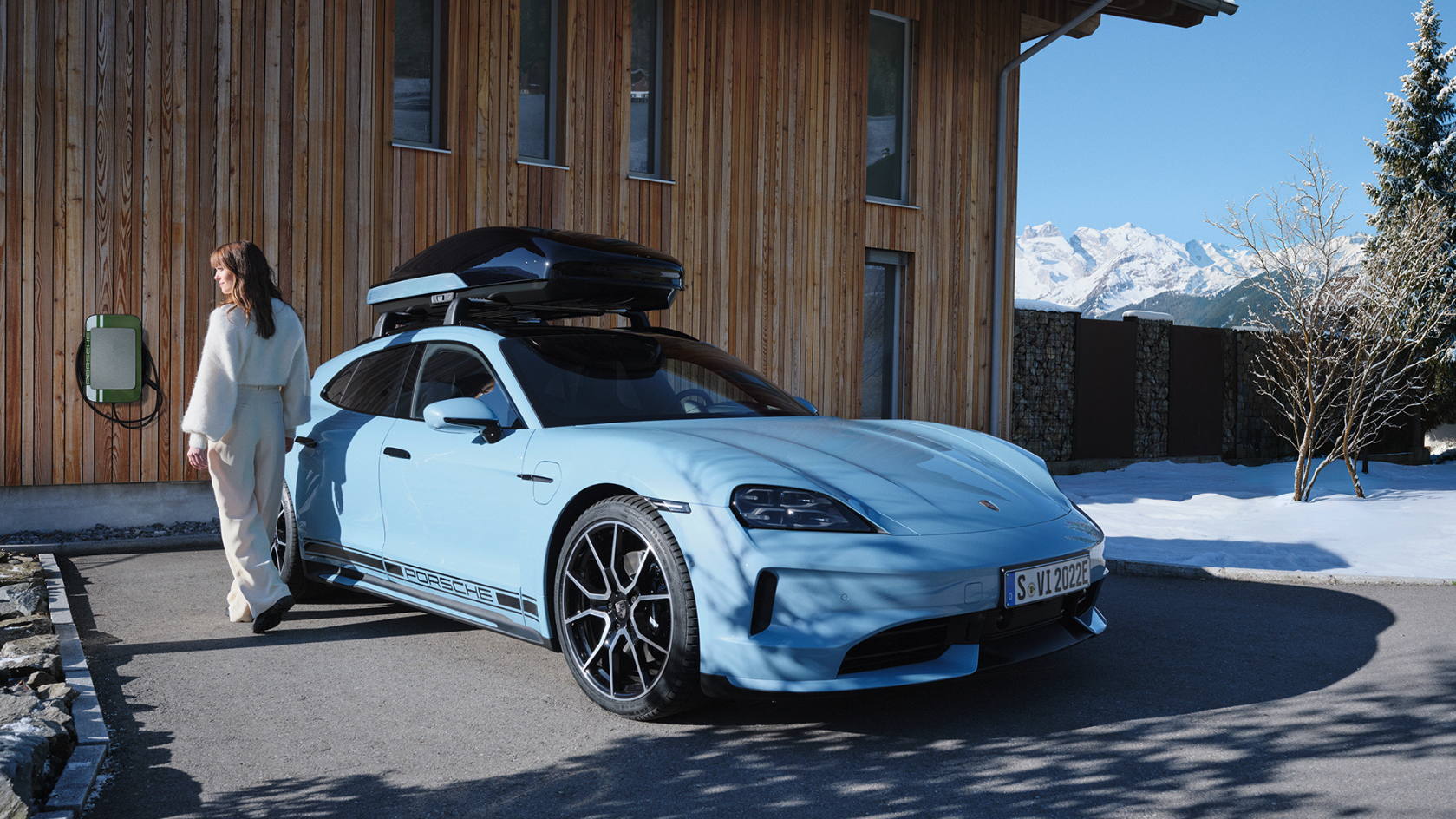 Porsche Taycan azul con cofre de techo junto a una casa de montaña