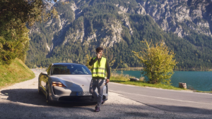 Persona con chaleco reflectante junto a un Porsche en carretera de montaña